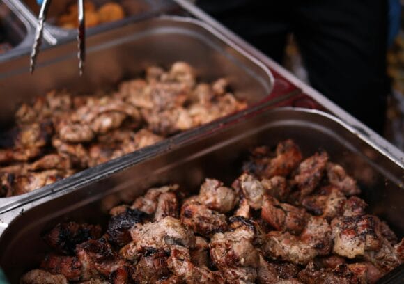A caterer wearing blue gloves uses tongs to serve grilled meat from a buffet tray at a wedding