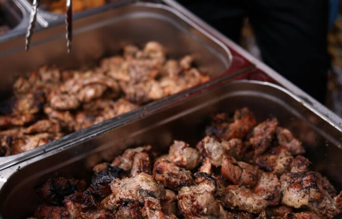 A caterer wearing blue gloves uses tongs to serve grilled meat from a buffet tray at a wedding