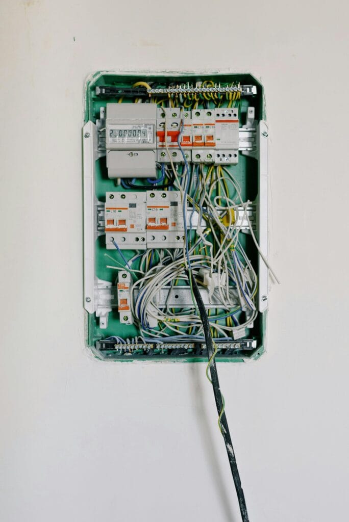 Wall-mounted electrical distribution board with multiple circuit breakers, an energy meter, and exposed wiring.