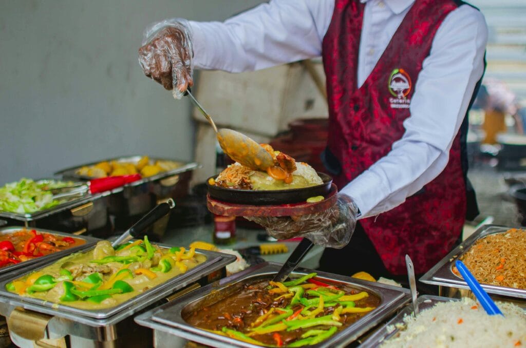 A professional caterer in uniform serving gourmet food from a buffet station at an upscale event in Kenya, showcasing premium catering services.